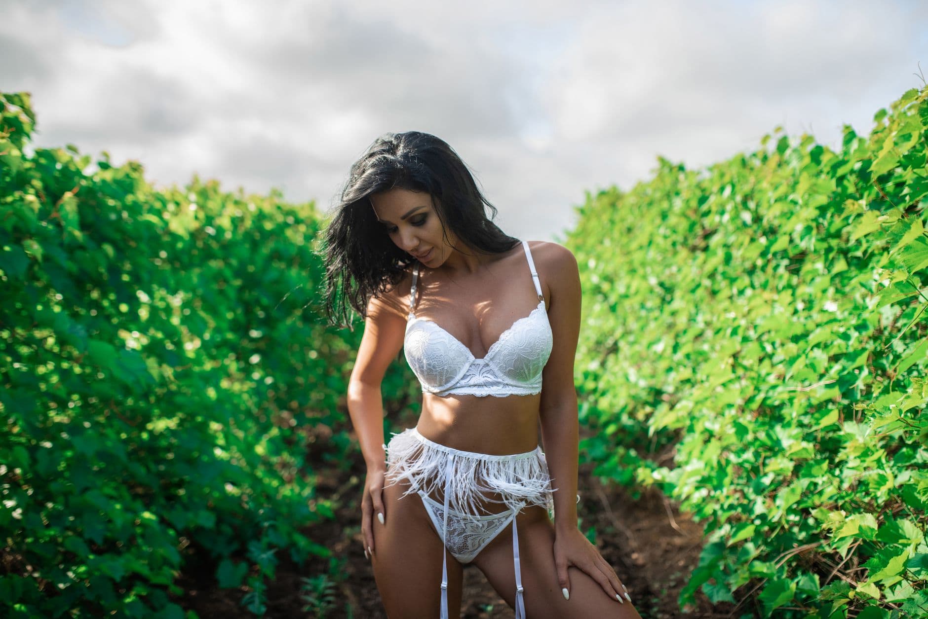 Woman in white lingerie amidst lush green vineyard during daytime.