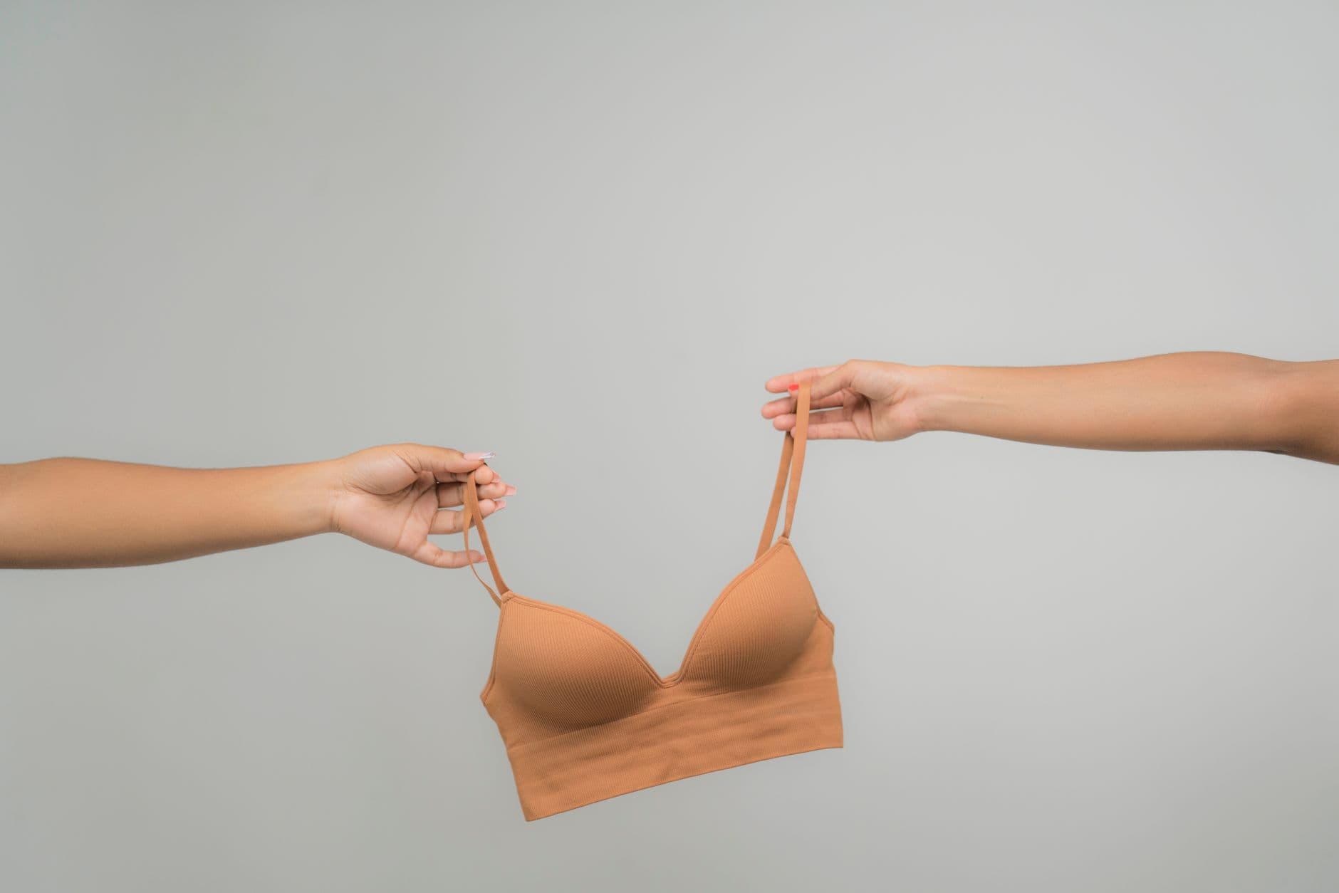 Two hands holding a nude bra against a light, neutral background, emphasizing fabric texture and design.